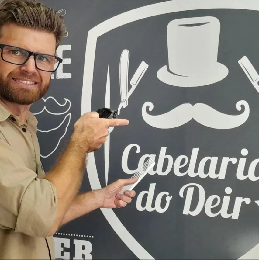 Deir apontando para o logo da Cabelaria do Deir na parede de lousa